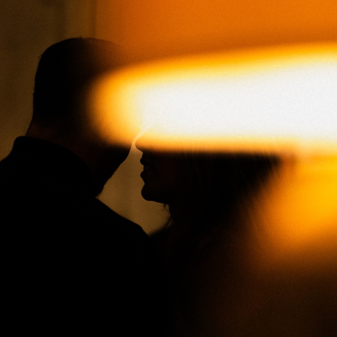 Two people in conversation, their faces crossed by a warm streak of light
